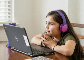 a little girl sitting at a table with a laptop