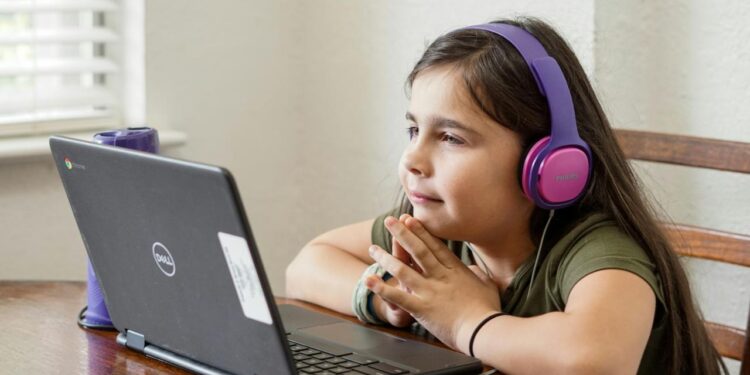 a little girl sitting at a table with a laptop